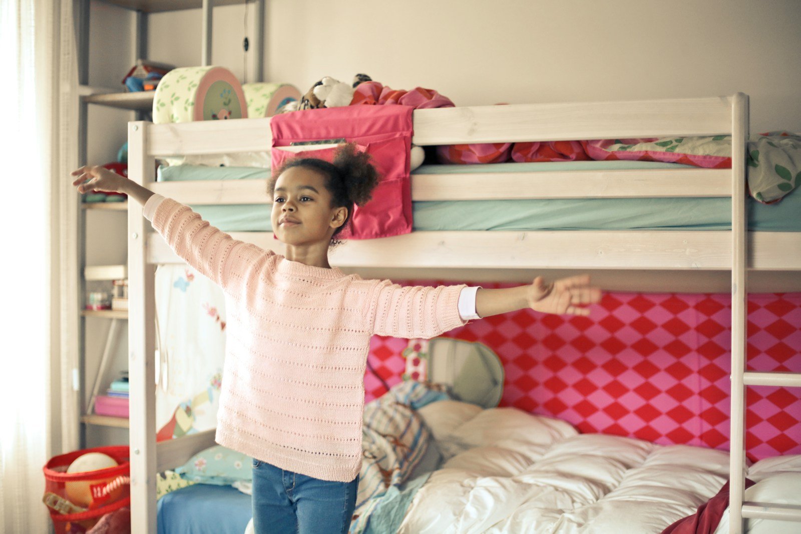 girl in white and red long sleeve shirt and blue denim jeans standing near bed